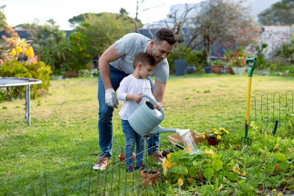 Happy father and son watering plants together. family time, having fun together at home and garden.
